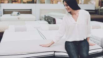 Mulher sentada em cima de um colchão numa loja de colchões para o como testamos da deco proteste.